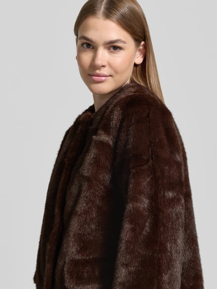 Frauenmodel trägt Webpelzmantel mit seitlichen Eingrifftaschen von LAUREN RALPH LAUREN in Braun, samtige Struktur, Nahaufnahme Oberkörper.