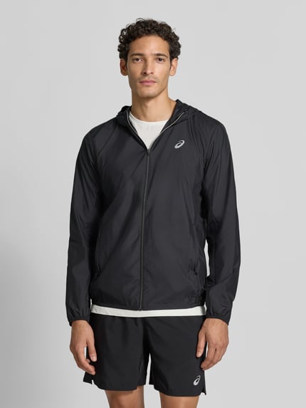 Männermodel trägt schwarze Regular Fit Trainingsjacke mit Logo-Print Modell 'Core' von ASICS TIGER, leichte Struktur, Ganzkörperansicht von vorne.
