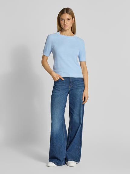 Frauenmodel trägt Regular Fit Strickpullover aus Viskose-Baumwoll-Mix Modell 'ELINNA' von Selected Femme in Hellblau, strukturierte Optik, Kurzarm, Rundhals, uni, Ganzkörperansicht von vorne.