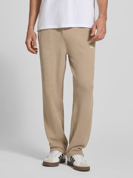 Männermodel trägt Wide Fit Sweatpants mit Label-Detail Modell 'Mezzano' von PEGADOR in Beige mit elastischem Bund, Eingrifftaschen, Ganzkörperansicht von vorne.