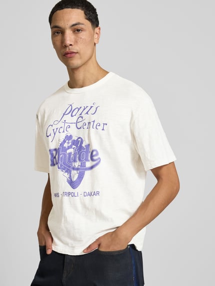 Männermodel trägt Regular Fit T-Shirt aus reiner Viskose von RHUDE mit Label-Print, weiß-lila, Nahaufnahme Oberkörper.
