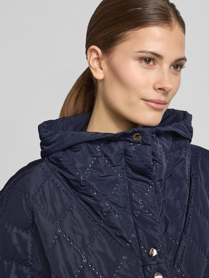 Vrouwenmodel draagt Cape met Steppnaden en steekzakken van Copenhagen Muse in donkerblauw met knoopsluiting, relaxed fit, hooggesloten kraag, detailopname bovenlichaam