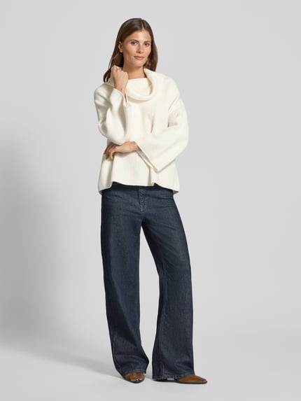 Frauenmodel trägt Strickpullover mit Rollkragen von comma in Offwhite, lockerer Schnitt, breite Ärmel, kombiniert mit Jeans, Ganzkörperansicht von vorne.