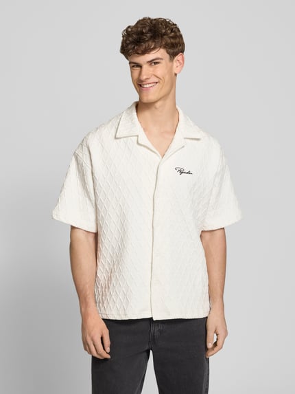 Männermodel trägt Regular Fit Freizeithemd mit Label-Stitching Modell 'Jovren' von Pegador, Reverskragen, Elastischer-Material-Mix, Halbarm, Knopfleiste, helle Farbe, strukturierte Oberfläche, Nahaufnahme Oberkörper. Rückenlänge bei Größe M: 72 cm, Schulterbreite: 45 cm, Ärmellänge: 33 cm.