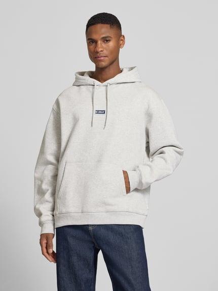 Männermodel trägt Hoodie mit Logo-Print Modell 'Chase' von Les Deux, Reine Baumwolle, Loose-Fit, Känguru-Tasche, Elastische Abschlüsse, Ganzkörperansicht von vorne.
