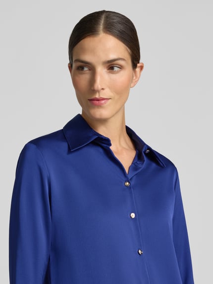 Frauenmodel trägt Slim Fit Bluse aus Satin Modell 'IDEALE' von MANGO in sattem Blau mit Hemdblusenkragen und Knopfleiste, Nahaufnahme Oberkörper.
