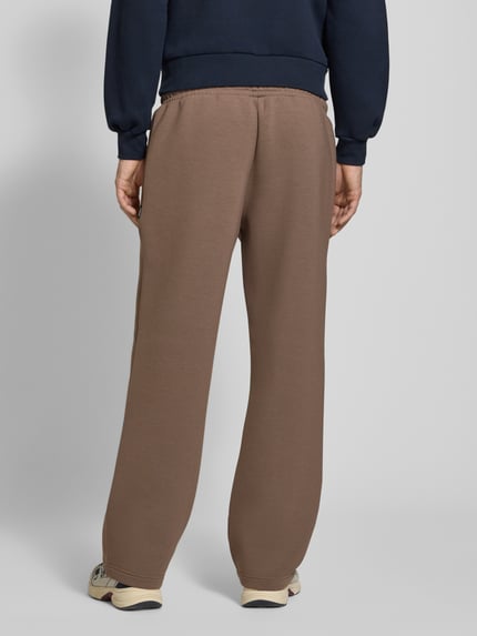 Männermodel trägt Regular Fit Sweatpants aus Material-Mix Modell 'BILL LEGACY' von JACK & JONES, braun, Elastikbund, Ganzkörperansicht Rückansicht, Herren Sweatpants, Eingrifftaschen, Innenbeinlänge 77 cm, KI-modifiziertes Bild.
