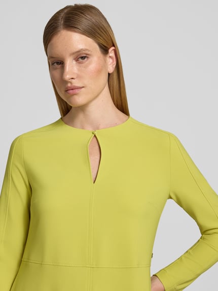 Frauenmodel trägt Damen Midikleid mit Schlüsselloch-Ausschnitt von Marc Cain aus Material-Mix mit Stretch-Anteil, Nahaufnahme Oberkörper. Rückenlänge bei Größe 36: 122 cm, Brustweite: 39 cm, Ärmellänge: 60 cm, A-Linie, Knopfverschluss, frische gelbe Farbe.