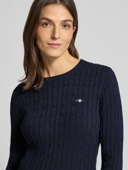 Kobiece model prezentuje granatowy Strickpullover mit Label-Detail od GANT z bawełnianej mieszanki, prążkowana faktura, jednolity kolor, zbliżenie na górną część ciała.