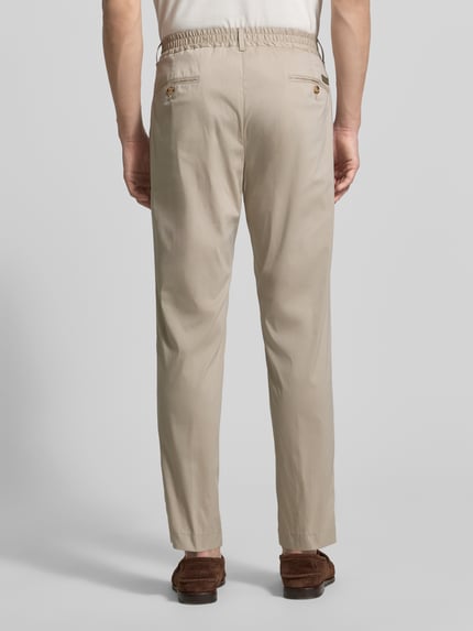 Männermodel trägt Regular Fit Stoffhose mit Logo-Detail Modell 'Lester' von JOOP! Collection in Beige, elastischer Baumwoll-Mix, Bundfalten, Gesäßtaschen, Ganzkörperansicht Rückansicht.