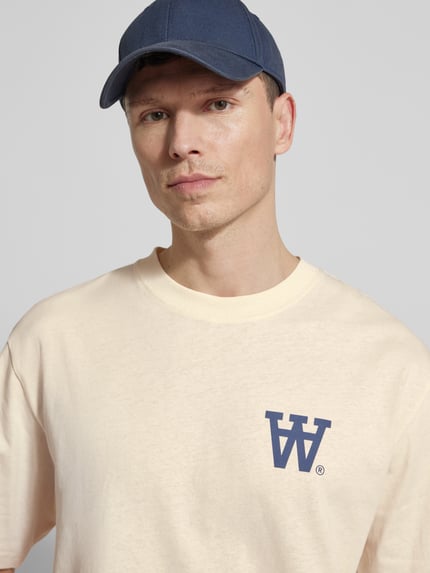 Männermodel trägt Relaxed Fit T-Shirt mit Logo-Print Modell 'Liam' von Wood Wood aus reiner Baumwolle, Rundhalsausschnitt, Nahaufnahme Oberkörper.