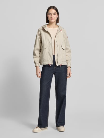 Vrouwenmodel draagt Jacke met Zweiwege-Reißverschluss Modell 'DOLORES NEO' van Frieda & Freddies in katoenmix, recht model, beige, met capuchon, labelpatch, klepzakken met knoopsluiting, elastische mouwboorden en verstelbare zoom, ruglengte bij maat 36: 59 cm, schouderbreedte: 48 cm, borstwijdte: 50 cm, mouwlengte: 52 cm. Volledige lichaamsaanzicht van voren.