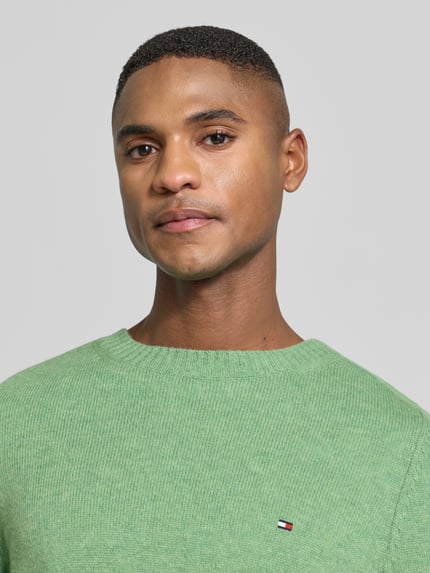 Männermodel trägt Regular Fit Strickpullover aus feinster Wolle von TOMMY HILFIGER, Optik: Unifarben, Logo-Detail, reine Baumwolle, Nahaufnahme Oberkörper.