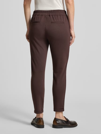 Frauenmodel trägt Skinny Fit Stoffhose mit Viskose-Anteil Modell 'NANNI' von FREE/QUENT in Braun, glatte Textur, Ganzkörperansicht Rückansicht. Elastischer Bund, verkürztes Bein, fixierte Beinabschlüsse, Produktdetails laut Kontext.