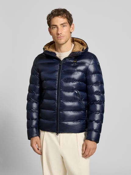 Männermodel trägt Steppjacke mit Zweiwege-Reißverschluss Modell 'ADAMS' von Blauer USA in Dunkelblau, glänzende Oberfläche, Ganzkörperansicht von vorne. Regular Fit, Kapuze mit Tunnelzug, Label-Detail, Rückenlänge 66 cm, Schulterbreite 44 cm, Brustweite 53 cm, Ärmellänge 65 cm.