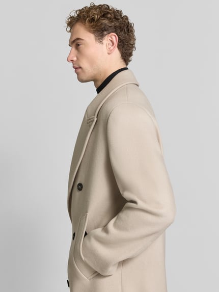 Männermodel trägt Zweireihiger Mantel aus Schurwoll-Mix mit Eingrifftaschen von bugatti in Beige, strukturierte Oberfläche, Ganzkörperansicht Seitenansicht. Regular Fit, Knopfverschluss, Reverskragen, Kaschmir-Anteil, dezente Farbtöne.
