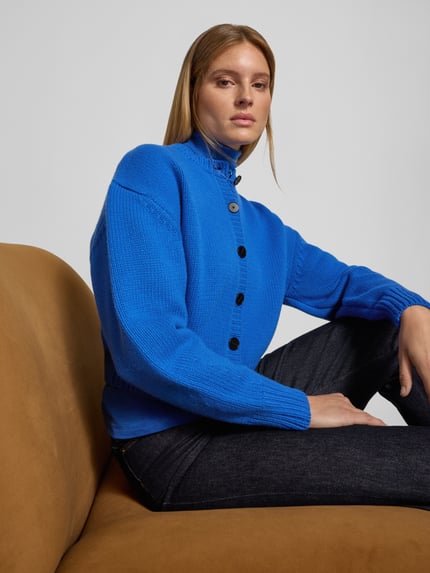 Frauenmodel trägt Knit Cardigan aus Wolle - curated by Viky Rader von Style Icon Collection in leuchtend Blau mit Knopfleiste und gerippten Abschlüssen aus reiner Baumwolle, lockere Passform, Rückenlänge 46 cm, Ärmellänge 58 cm, Nahaufnahme Oberkörper.