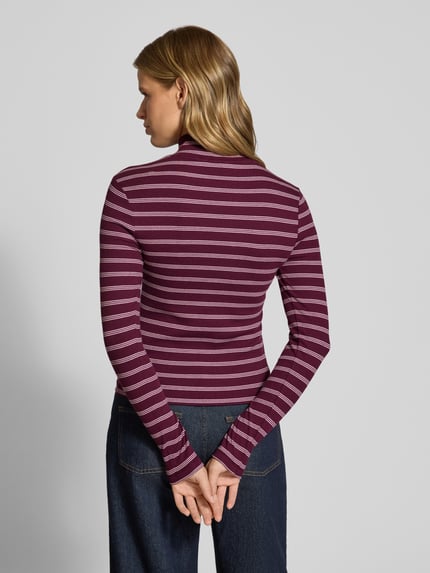 Frauenmodel trägt Slim Fit Langarmshirt aus Baumwoll-Mix von Tommy Jeans in lila mit weißen Streifen, glatte Textur, Ganzkörperansicht Rückansicht. Damen Langarmshirt von Tommy Jeans