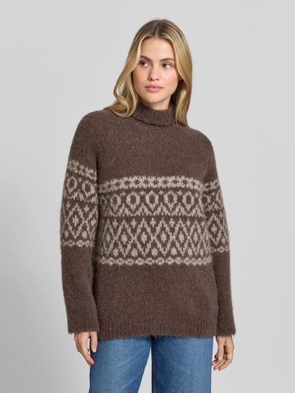Frauenmodel trägt Pullover aus Alpaka mit Rollkragen Modell 'CRISTINE' von BAUM & PFERDGARTEN in brauner Strickoptik mit geometrischem Jacquard-Muster, gerippte Abschlüsse, langarm, Ganzkörperansicht von vorne.