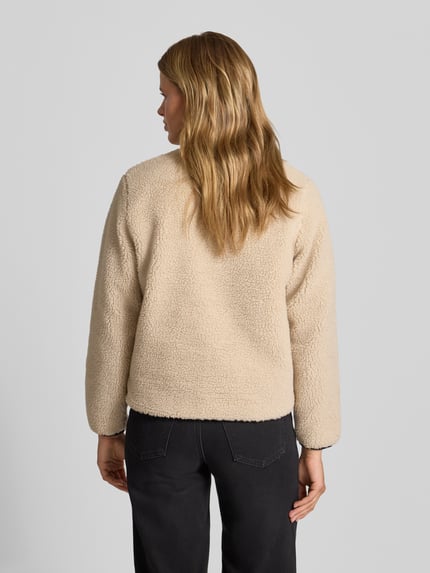 Frauenmodel trägt Fleecejacke mit Zweiwege-Reißverschluss Modell 'Janet' von Carhartt Work In Progress in Beige, Teddyfell-Textur, Ganzkörperansicht Rückansicht. Damen Fleecejacke, Regular Fit, Stehkragen, Eingrifftaschen, Brusttasche, Label-Detail.