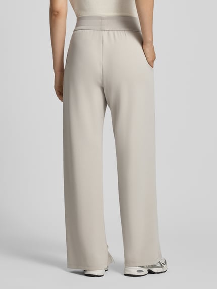 Frauenmodel trägt Straight Fit Sweatpants aus elastischem Viskose-Mix von Armani Exchange in Beige, elastischer Bund, Bein-Schlitze, Ganzkörperansicht Rückansicht.
