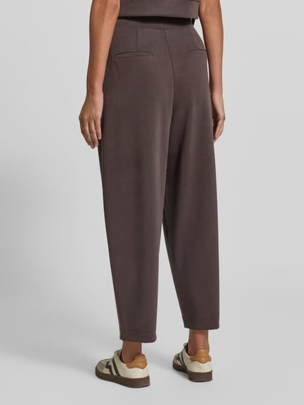 Frauenmodel trägt Sweatpants aus Modal-Mix mit Bundfalten von Rich & Royal in Dunkelbraun, strukturierte Oberfläche, Ganzkörperansicht Rückansicht. Damen Sweatpants von Rich & Royal, Modal-Mix mit Stretch-Anteil, Barrel Fit, Bundfalten, elastischer Bund, Gesäßtaschen, Innenbeinlänge bei Größe S: 70 cm.
