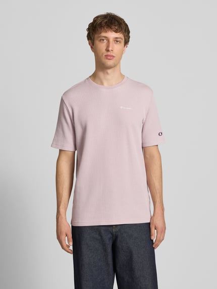 Männermodel trägt T-Shirt mit Strukturmuster und Label-Stitchings von CHAMPION in zartem Rosa, Baumwoll-Mix, Regular-Fit, Ganzkörperansicht von vorne. Rückenlänge bei Größe M: 68 cm.