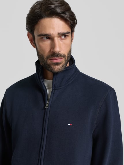 Männermodel trägt Regular Fit Sweatjacke aus Baumwoll-Mix von Tommy Hilfiger in Dunkelblau mit Stehkragen und Label Stitching, Nahaufnahme Oberkörper.