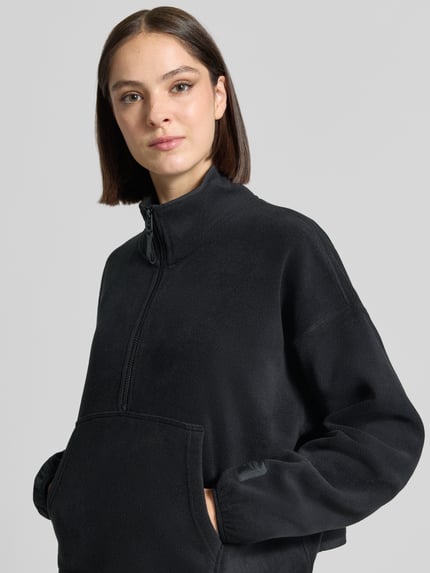 Frauenmodel trägt Relaxed Fit Pullover Troyer-Kragen Modell 'Polar' von Fabletics, Damen Fleecejacke in Schwarz mit Kängurutasche, Nahaufnahme Oberkörper.