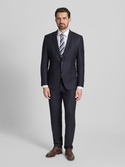 Männermodel trägt Slim Fit Businesshemd mit extra langem Arm von Jake*s in Weiß, kombiniert mit dunklem Anzug, Ganzkörperansicht von vorne. Hemd aus reiner Baumwolle, Kentkragen, Knopfleiste, schlichte Struktur.
