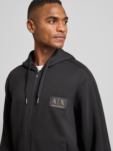 Męskimodel nosi Bluza rozpinana z zamkiem błyskawicznym dwustronnym od Armani, mieszanka materiałów z modalu, krój regular fit, kaptur, naszywka z logo, wpuszczane kieszenie, czarna, tekstura gładka, długość tyłu 68 cm, długość rękawów 61 cm, nahaufnahme górnej części ciała.