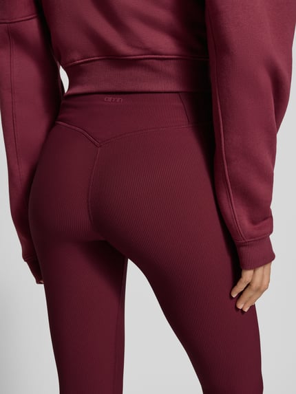 Frauenmodel trägt bordeauxrote AIMN Leggings mit elastischem Bund, gerippte Textur, körpernahe Passform, Nahaufnahme Rückansicht.