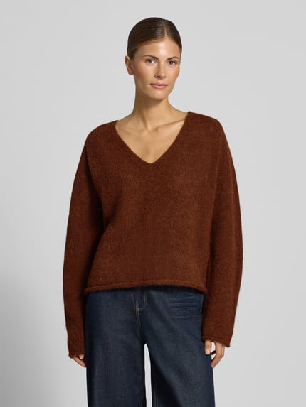 Frauenmodel trägt Relaxed Fit Strickpullover aus Alpaka-Mix Modell 'SOMAIJA' von DRYKORN in Braun, grobe Textur, Nahaufnahme Oberkörper. Damen Strickpullover, V-Ausschnitt, Rollsaum, Rückenlänge 55 cm, Ärmellänge 60 cm.