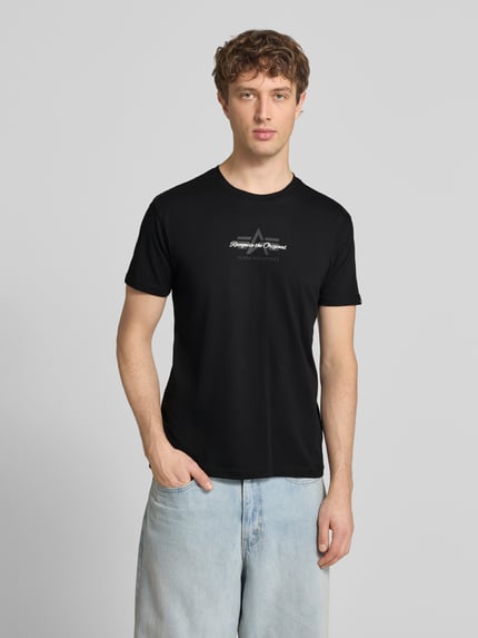 Männermodel trägt schwarzes Herren T-Shirt mit Label-Detail Modell 'Foam' von Alpha Industries aus Reine Baumwolle, Gerader-Schnitt, Rundhalsausschnitt, Label-Details, Rückenlänge bei Größe M 67 cm, Ganzkörperansicht von vorne.