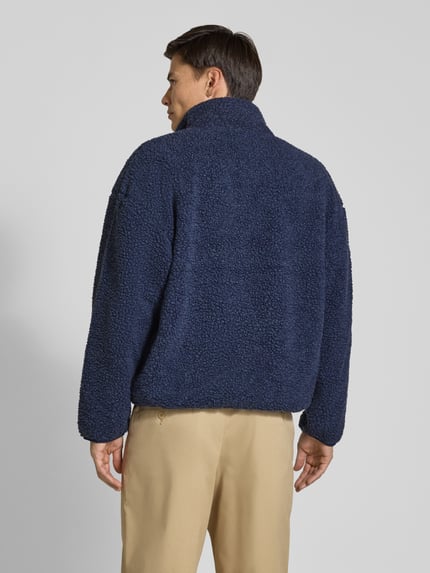 Männermodel trägt unifarbene, strukturierte Sweatjacke mit Logo-Patch Modell 'HOKTOWN' von AMERICAN VINTAGE in Dunkelblau, Fleece-Textur, Ganzkörperansicht Rückansicht.