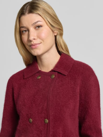 Frauenmodel trägt Strickjacke aus reiner Wolle von Christian Berg Woman in Bordeaux mit Umlegekragen und Knopfleiste, Nahaufnahme Oberkörper.