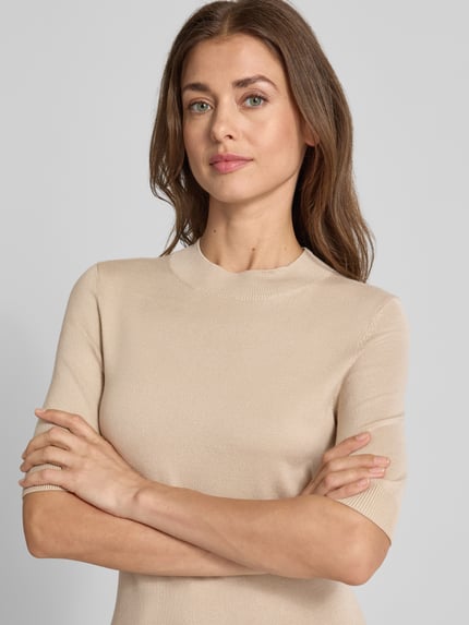 Frauenmodel trägt Slim Fit Strickpullover aus Viskose-Mix von COMMA in Beige mit gerippter Blende, Halbarm, Nahaufnahme Oberkörper.