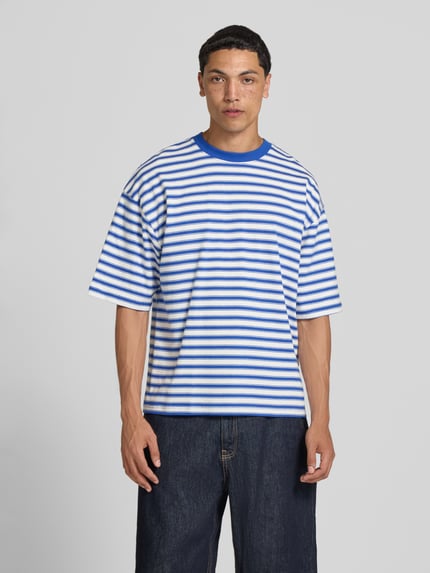 Männermodel trägt Oversized T-Shirt mit Label-Stitching von REVIEW, blaue und weiße Streifen, Reine Baumwolle, Allover-Look, Rundhalsausschnitt, Rückenlänge bei Größe M 67 cm, Ganzkörperansicht von vorne.