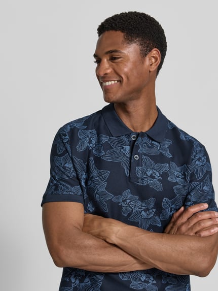 Männermodel trägt Slim Fit Poloshirt mit floralem Allover-Print von Lerros aus Reiner Baumwolle, dunkelblau, Nahaufnahme Oberkörper.