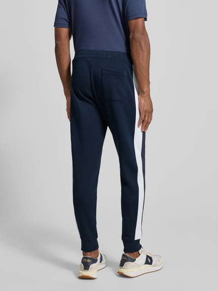Männermodel trägt Sweatpants mit elastischem Bund von Polo Ralph Lauren, Herren, Baumwoll-Mix, lockerer Schnitt, Reißverschlusstaschen, Gesäßtasche, Farbe Dunkelblau mit weißem Streifen, Ganzkörperansicht Rückansicht.