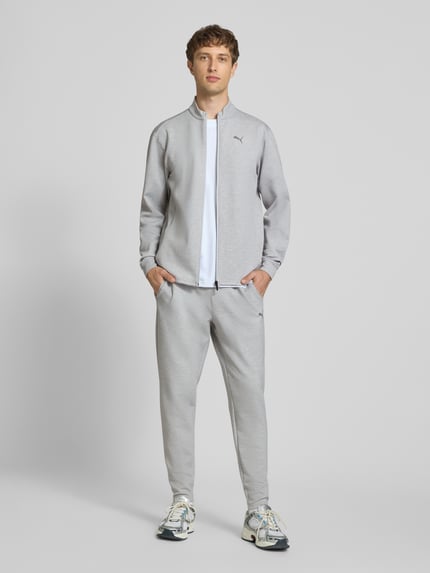 Männermodel trägt Sweatjacke mit Stehkragen und Logo von PUMA PERFORMANCE, grau, Regular Fit, Reißverschluss, Ganzkörperansicht von vorne.