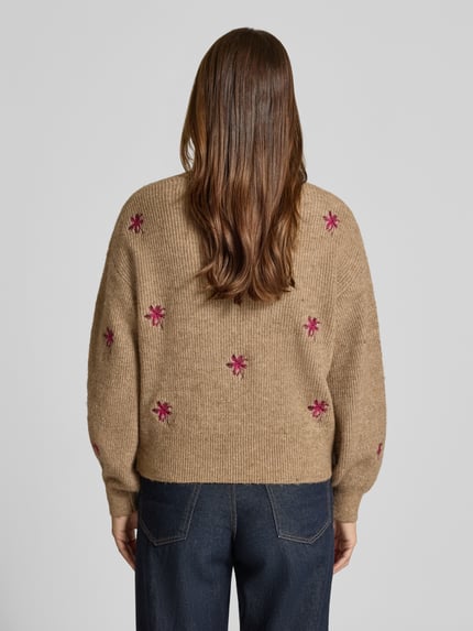 Vrouwenmodel draagt cardigan met oversneden schouders model 'FLEUR' van YAS, materiaalmix met katoen, loose fit, V-hals, knoopsluiting, ruglengte maat S 52 cm, mouwlengte maat S 52 cm, beige met roze geborduurde bloemen, ribtextuur, denim broek, volledige rugaanzicht