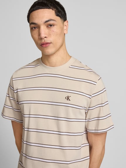 Männermodel trägt T-Shirt mit Logo-Stitching von Calvin Klein Jeans in Beige mit braunen Streifen, Reine Baumwolle, Gerader-Schnitt, Rundhalsausschnitt, Rückenlänge bei Größe M 69 cm, Nahaufnahme Oberkörper