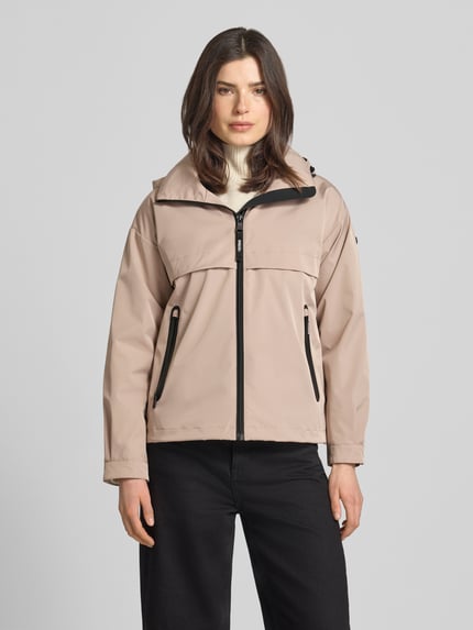 Vrouwenmodel draagt Jacke mit Stehkragen van khujo in beige met zwarte ritssluitingen, regular fit, ritszakken, opstaande kraag, ruglengte maat S 60 cm, schouderbreedte 51 cm, borstwijdte 50 cm, mouwlengte 54 cm, volledig zichtbaar van voren
