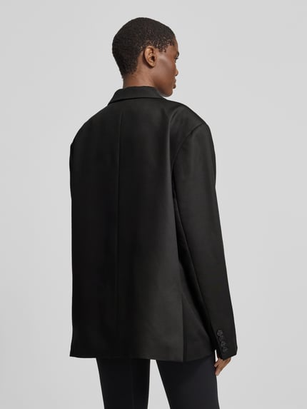 Frauenmodel trägt Regular Fit Longblazer mit Label-Detail von black palms, unifarben, Reverskragen, Pattentaschen, Ganzkörperansicht Rückansicht.