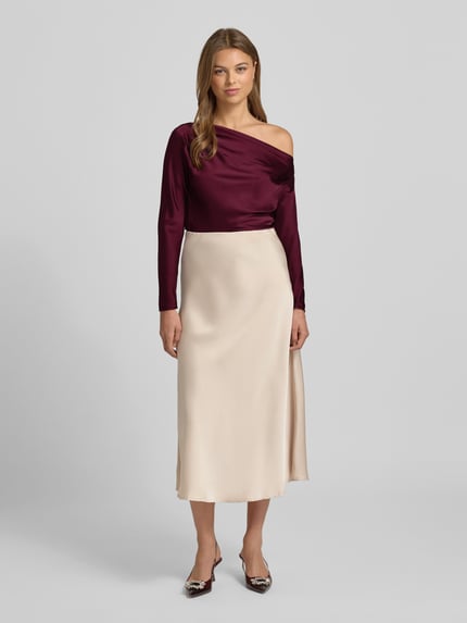 Frauenmodel trägt Regular Fit Bluse im One-Shoulder-Look Modell 'HASBRIN' von Lauren Ralph Lauren aus bordeauxfarbenem Satin, kombiniert mit cremefarbenem Rock, ganzkörperansicht von vorne. Rückenlänge bei Größe S 52 cm, Ärmellänge bei Größe S 63 cm.