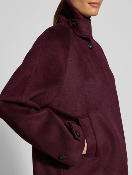 Kobieta nosi kurtkę 'Jacke mit Woll-Anteil' od Christian Berg Woman Selection, mieszanka materiałów z dodatkiem wełny, śliwkowy kolor, wpuszczane kieszenie, prosty krój, patki przy mankietach, plisa z zapięciem na guziki, wykładany kołnierz, zbliżenie na górną część ciała z przodu.