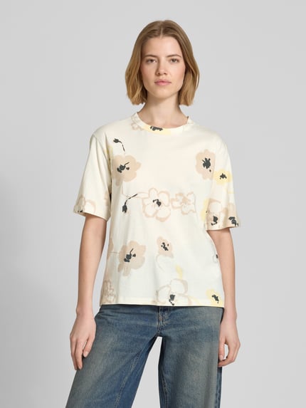 Modelka kobieca nosi T-Shirt im Allover-Look mit Rundhalsausschnitt od JAKE*S STUDIO WOMAN, czysta bawełna, krój regular fit, wzór allover, długość pleców w rozmiarze S: 57 cm, jasne kolory, motyw kwiatowy, widok całej sylwetki z przodu.