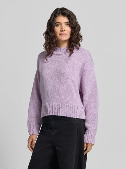 Kobiece modelka nosi sweter wełniany 'Pullover aus Wolle Alpaka mit Rippbündchen' od MARC CAIN, krój regular fit, efekt: jednolity kolor, imitacja dzianiny, długość: krój krótki, luźne ramiona, okrągły dekolt, rękaw: długi, zakończenia rękawów i dołu prążkowane, widok całej sylwetki z przodu.