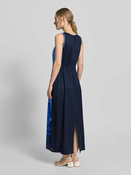Vrouwenmodel draagt Maxikleid aus reinem Lyocell mit Allover-Foto-Print van Marc Cain, donkerblauw met blauwe details, getailleerd, mouwloos design, ronde hals, all-over fotoprint, ruglengte maat 36: 134 cm, borstwijdte maat 36: 47 cm, geheel in beeld, rugaanzicht.